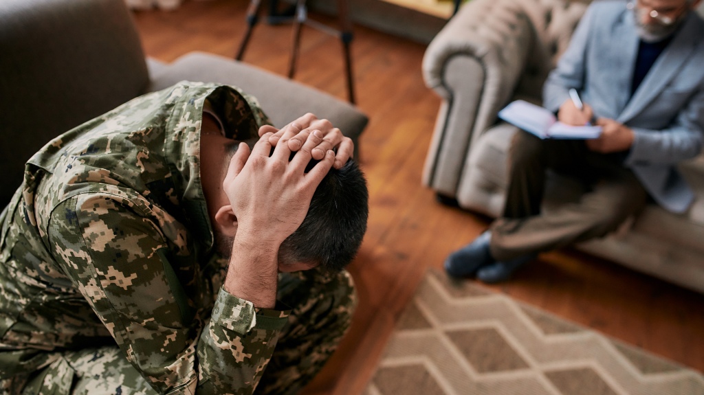 Middle aged military man holding his head in pain and depression during therapy session