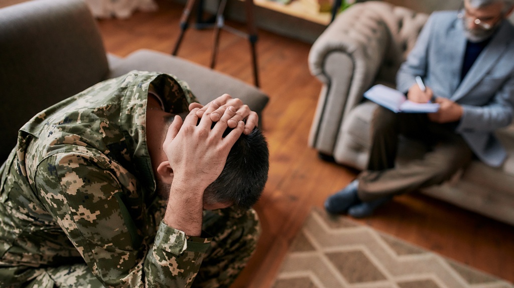 military man holding his head in pain and depression during therapy session with psychologist
